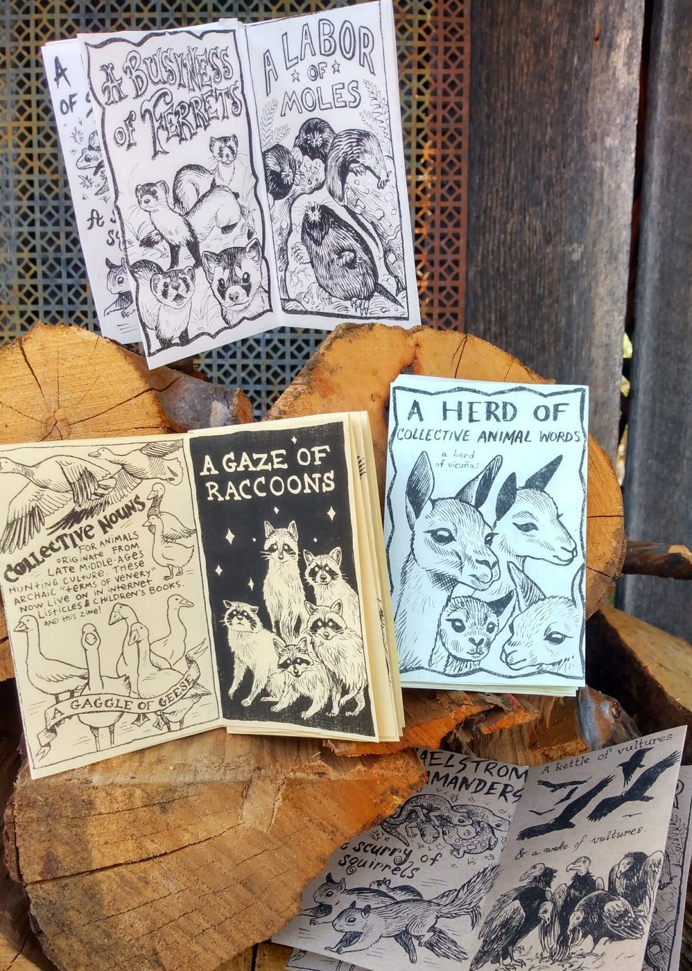 A small pile of mini-zines featuring animal drawings are displayed on a woodpile.