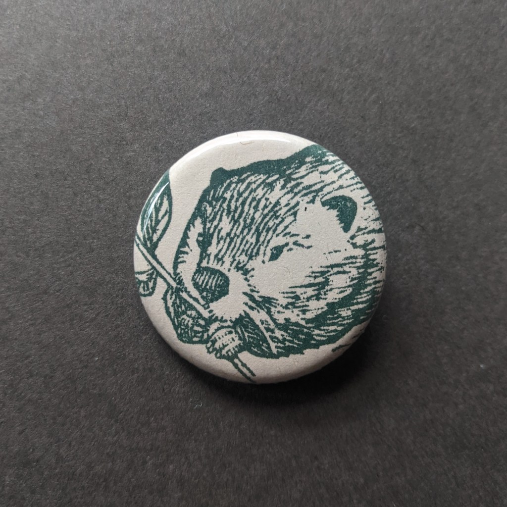a pinback button, stamped with a hand-carved stamp of a green beaver