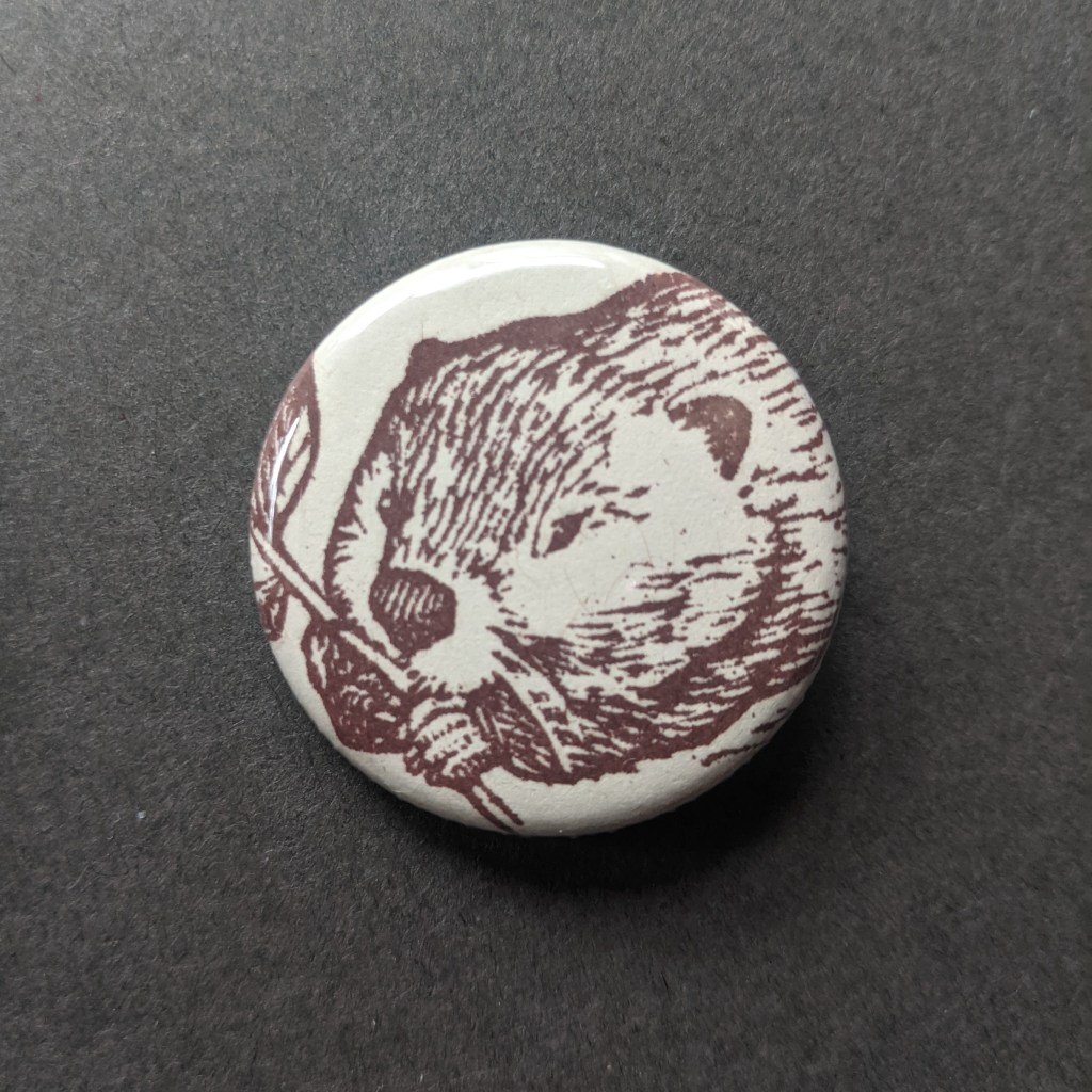 a pinback button, stamped with a hand-carved stamp of a brown beaver