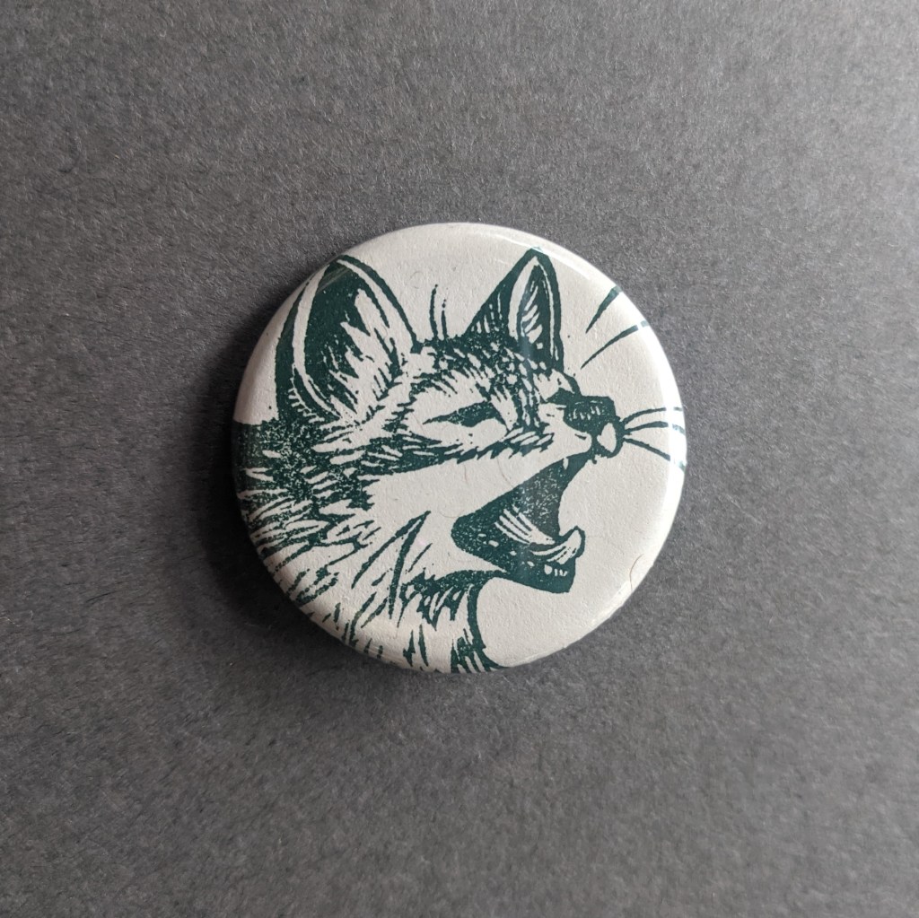 a pinback button, stamped with a hand-carved stamp of a fox yawning