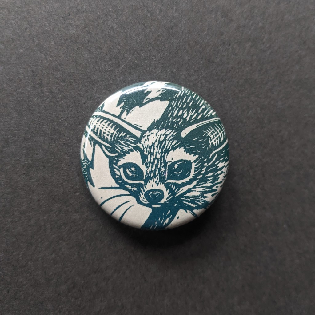 a pinback button, stamped with a hand-carved stamp of a ringtail cat