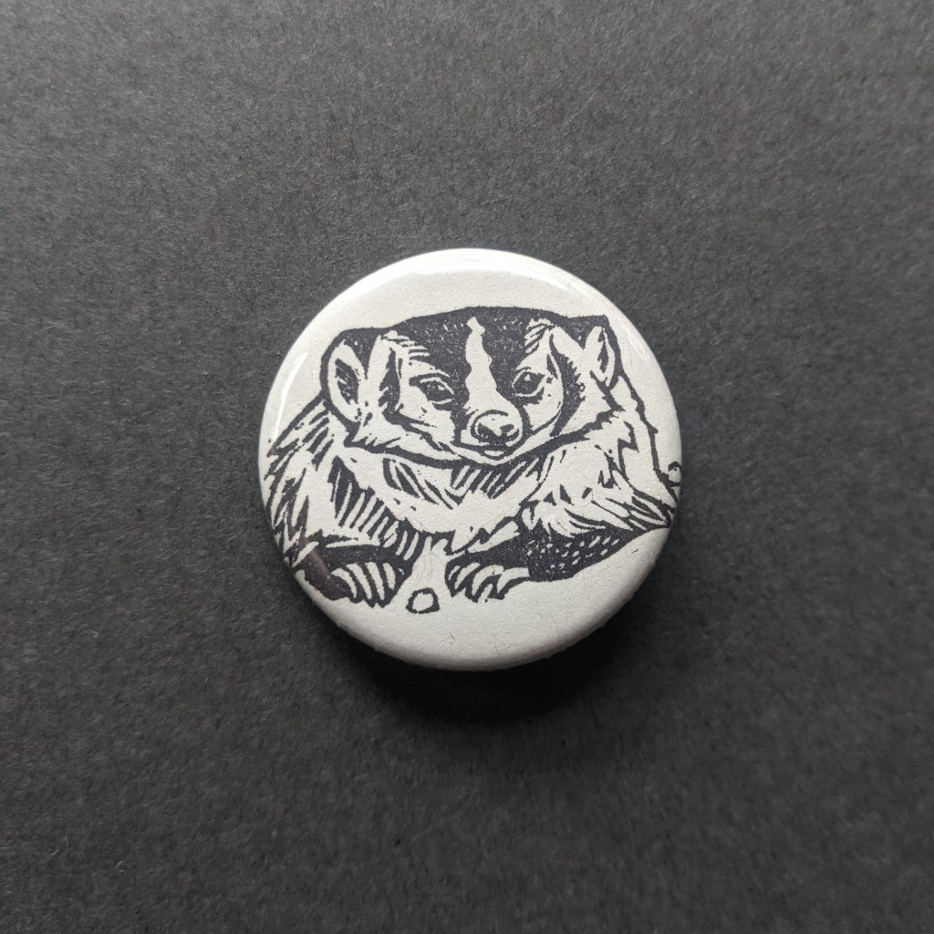a pinback button, stamped with a hand-carved stamp of an american badger