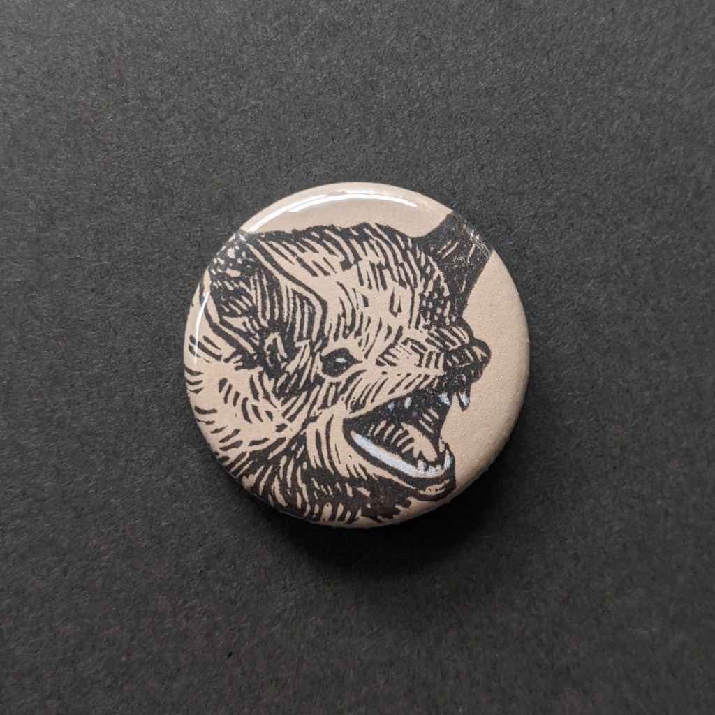 a pinback button, stamped with a hand-carved stamp of a bat face