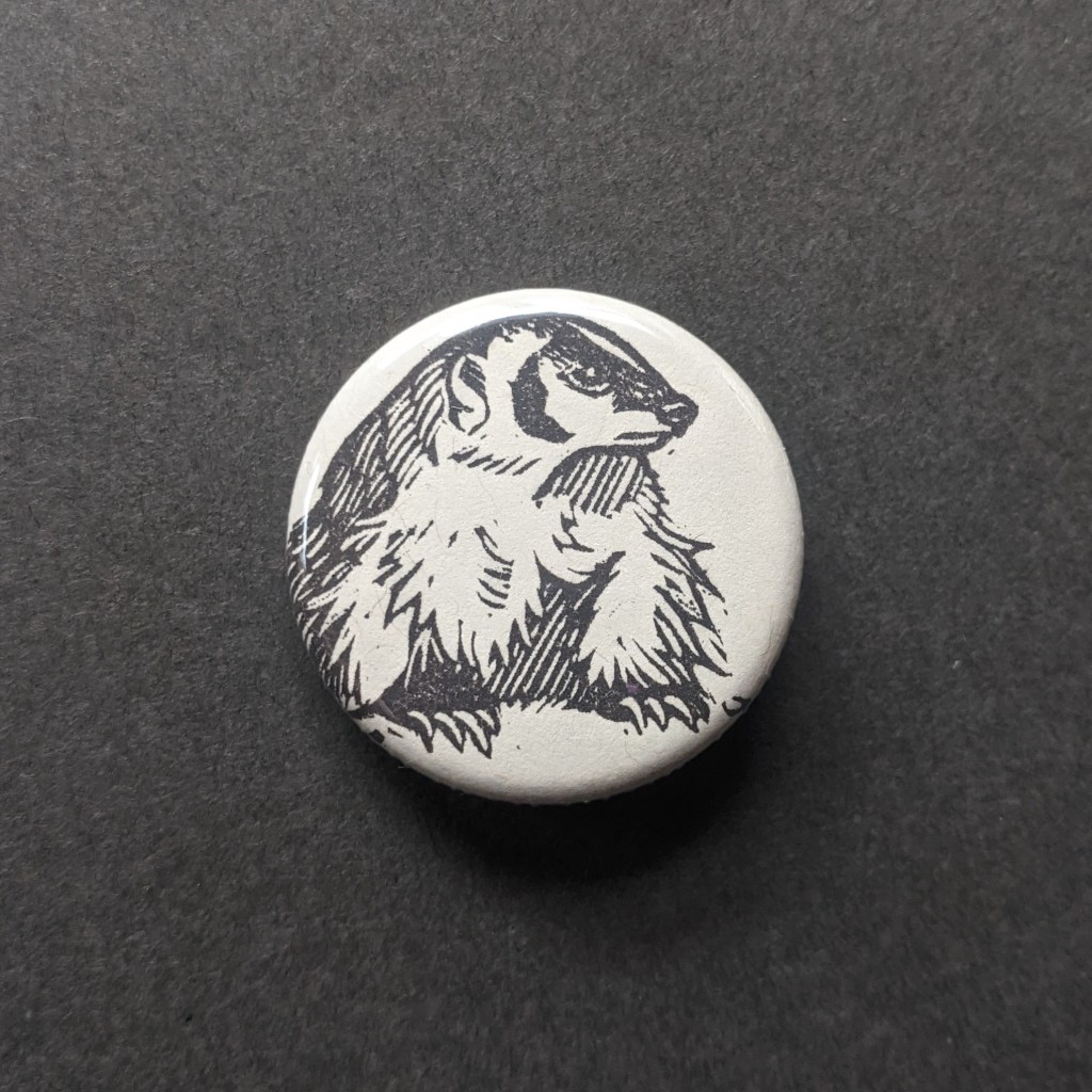 a pinback button, stamped with a hand-carved stamp of a badger