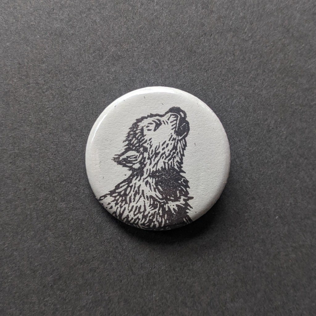 a pinback button, stamped with a hand-carved stamp of a wolf pup howling