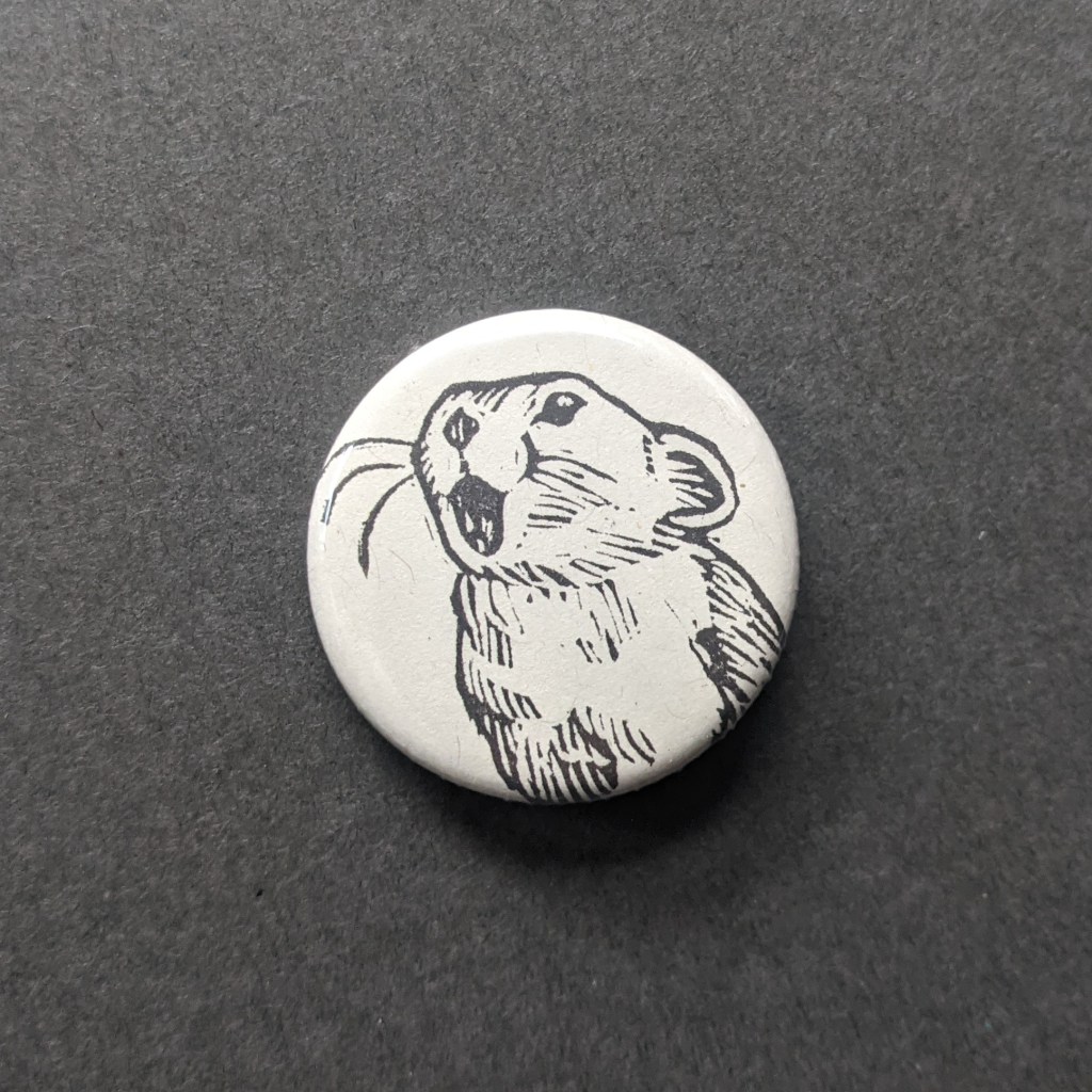a pinback button, stamped with a hand-carved stamp of a pika