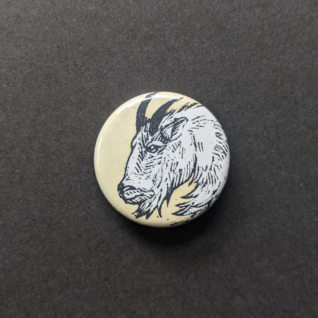 a pinback button, stamped with a hand-carved stamp of a mountain goat