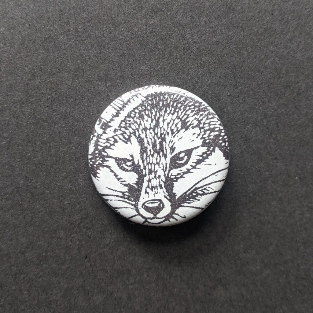 a pinback button, stamped with a hand-carved stamp of a realistic fox face