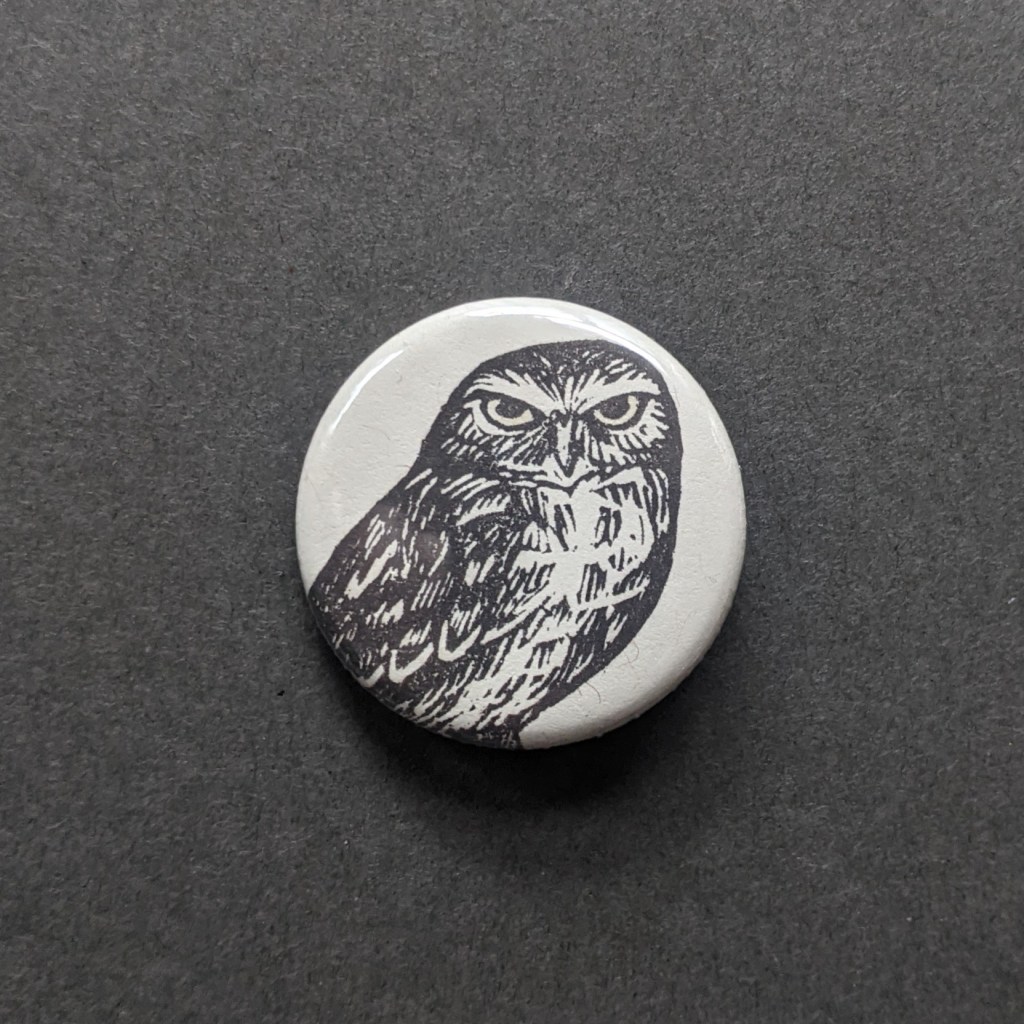 a pinback button, stamped with a hand-carved stamp of a burrowing owl