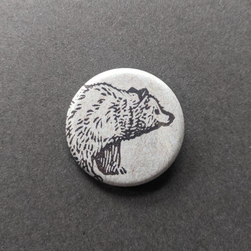 a pinback button stamped with a bear