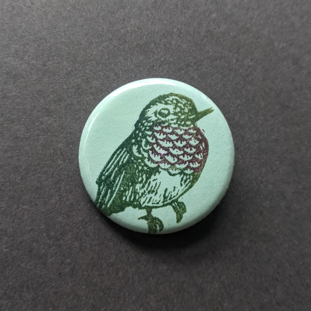 a green button with a stamp of a hummingbird
