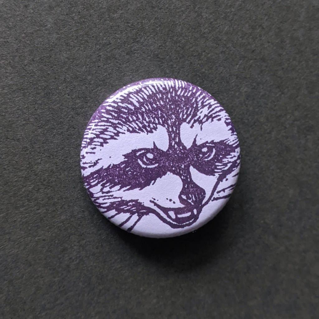 a pin button of a hand stamped raccoon face, from a hand carved stamp